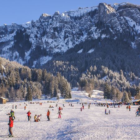 Schneepiste an einem sonnigen Tag mit vielen Besuchen und im Hintergrund sind die Berge zu sehen