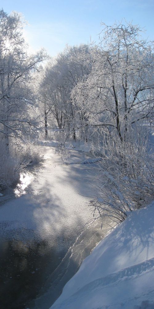 Zugefrorener Fluss mit eingeschneiter Landschaft drumherum